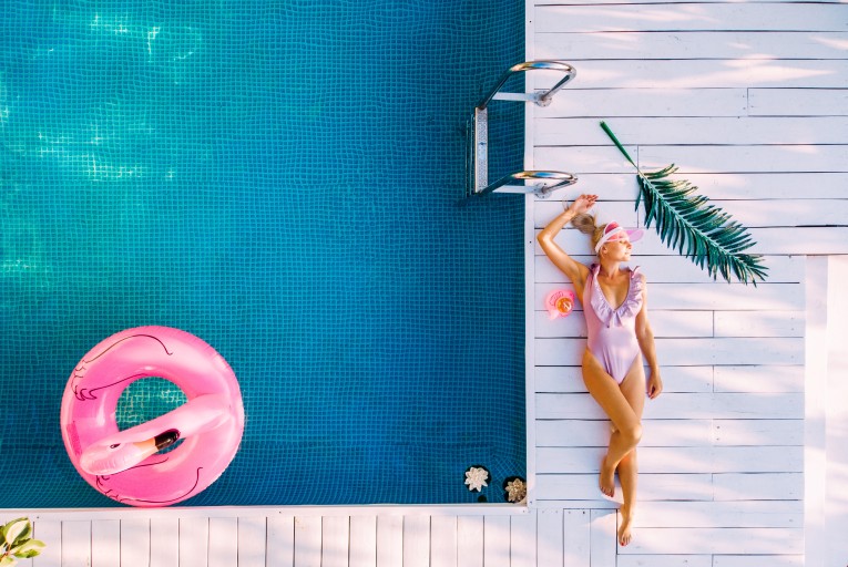 A woman in a pink bikini is enjoying a pink float in a swimming pool designed by a custom pool installation company in Minneapolis.